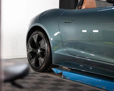 Close-up of a sleek car's rear wheel and side panel with a leather seat visible.