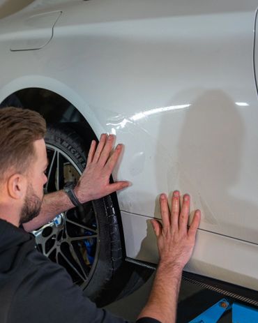Man applying protective film on white car's rear fender.