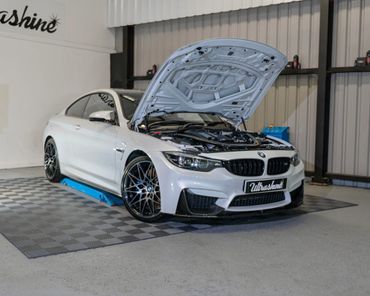 White BMW car with open hood in a garage.