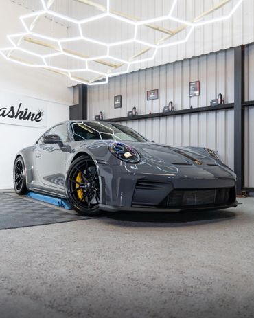 A sleek grey Porsche sports car in a modern showroom with geometric ceiling lights.