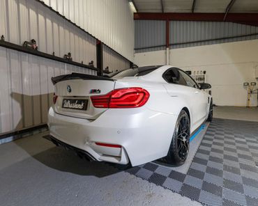 White BMW M4 Competition parked indoors with black wheels and a carbon spoiler.