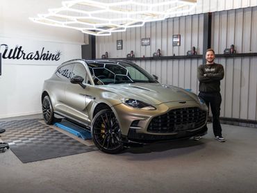 Man stands proudly next to a sleek luxury car in a showroom.
