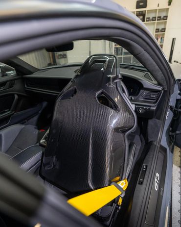 Carbon fiber racing seat with a yellow seatbelt inside a Porsche GT3.