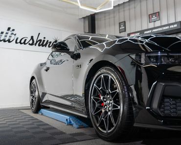 Shiny black sports car with detailed rims in a garage.