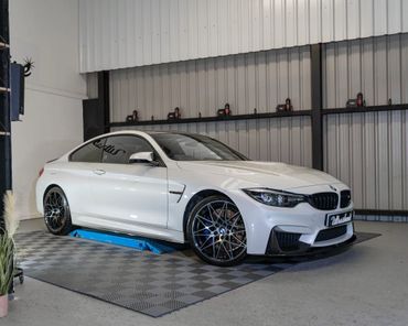 White BMW coupe parked in a showroom with black wheels and tinted windows.