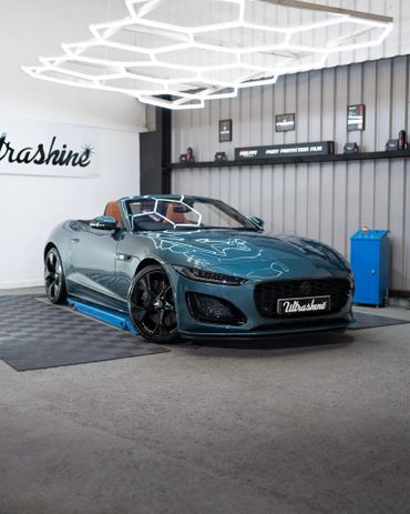 A sleek teal convertible sports car in a modern garage with bright hexagonal ceiling lights.