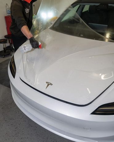 Person applying protective film on a white Tesla car hood.