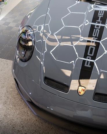 Close-up of a gray Porsche GT3 hood with reflections and logo.