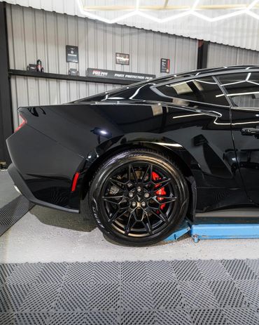 Close-up of a sleek black car's rear wheel with red brake calipers in a garage.