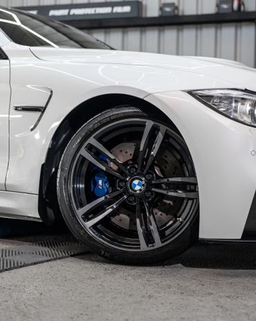 Close-up of a white BMW M4 wheel with black rim and blue brake caliper.