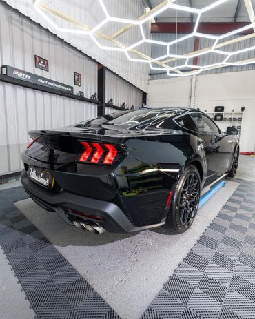 Sleek black sports car with glowing red taillights in a modern garage.