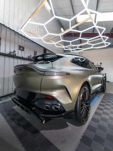 Rear view of a sleek Aston Martin SUV under futuristic lighting.