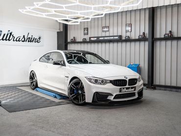 Sleek white BMW M4 with black rims in a modern garage showroom.