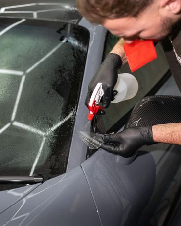 Man applying protective film on a car window using spray and squeegee.