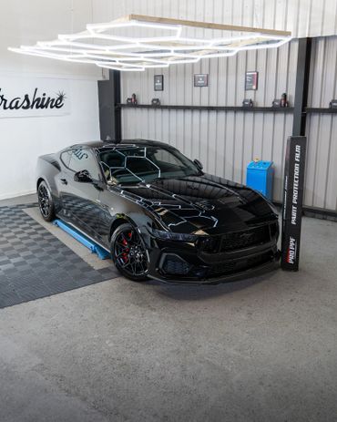 Glossy black sports car under geometric ceiling lights in a modern garage.
