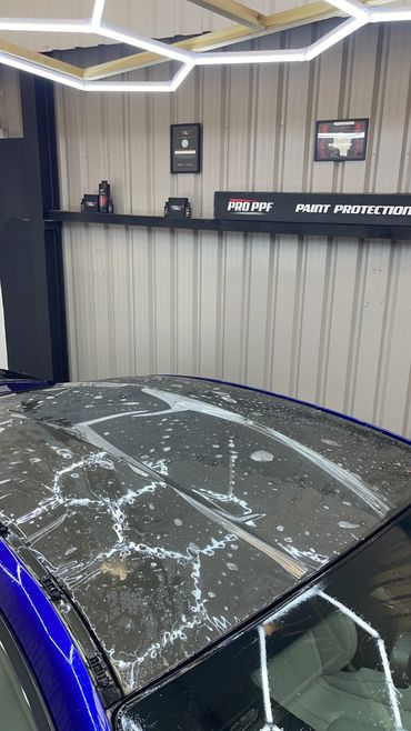 Car roof being covered with paint protection film in a workshop.