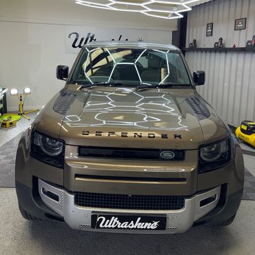 Front view of a Land Rover Defender under hexagonal LED lights in a garage.