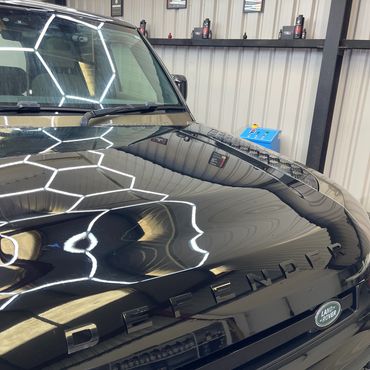 Shiny black Land Rover Defender with hexagonal ceiling light reflections.
