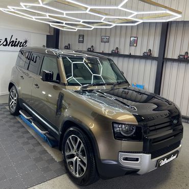 Shiny Land Rover Defender under modern hexagonal lights in a showroom.