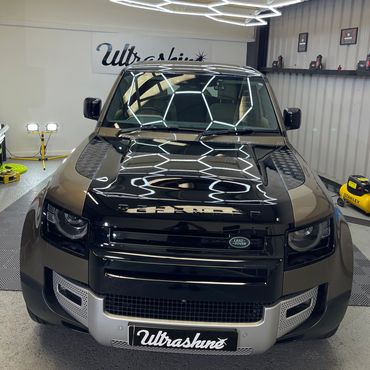 Black Land Rover Defender under hexagonal LED lighting in a detailing studio.
