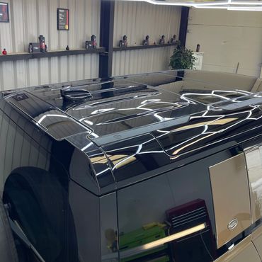 Glossy black Land Rover roof reflecting geometric ceiling lights.