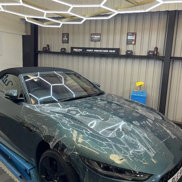 Luxury car undergoing paint protection film application in a well-lit garage.
