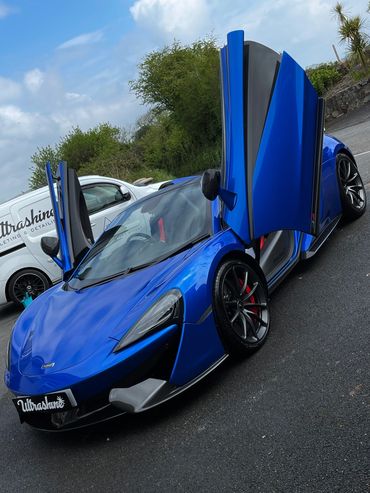 Blue McLaren sports car with butterfly doors open on asphalt.