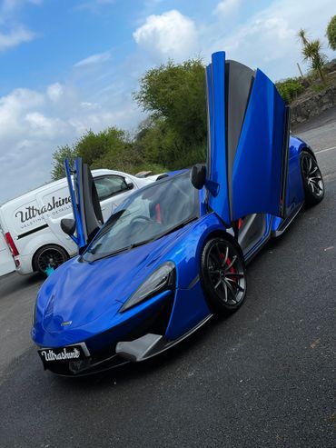 Blue McLaren sports car with butterfly doors open on asphalt.