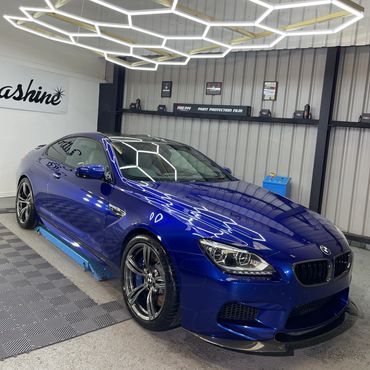 Sleek blue BMW car under modern hexagonal ceiling lights in a garage.