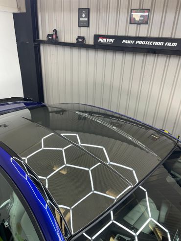 Close-up of a car's carbon fiber roof with hexagonal light reflections.