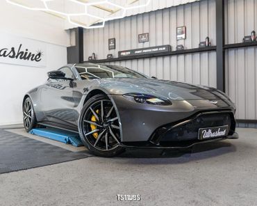 Sleek gray Aston Martin sports car inside a detailing garage.