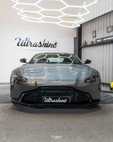 Sleek gray Aston Martin sports car with reflective geometric ceiling lights.