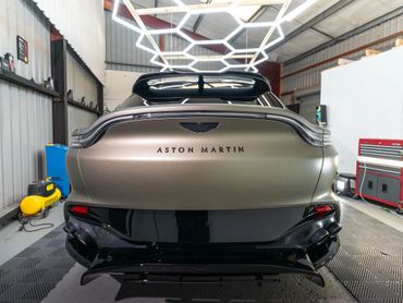 Rear view of a matte gold Aston Martin car inside a garage.