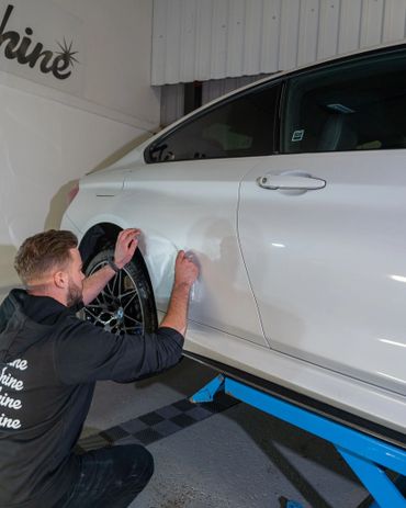 Man applying protective film on white car's rear side panel.