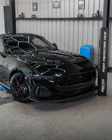 A sleek black Ford Mustang with red brake calipers in a garage.