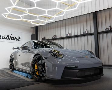 A sleek gray Porsche sports car inside a modern garage with hexagonal ceiling lights.
