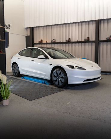 White Tesla Model 3 parked indoors on a blue lift platform.