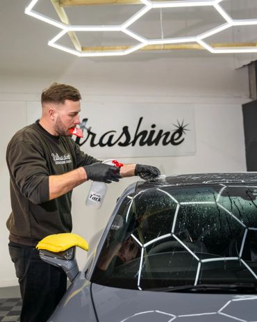 Man applying protective film on car windshield with spray and squeegee.