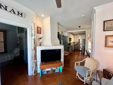 Cozy living space with white brick fireplace, wooden floors, and a modern kitchen in the background.