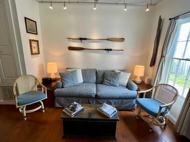 Cozy living room with blue sofa, wooden chairs, and nautical decor.