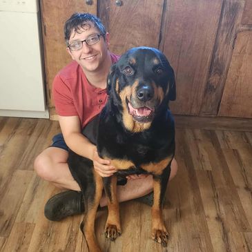 Man sitting on the floor hugging a happy Rottweiler dog in a kitchen.