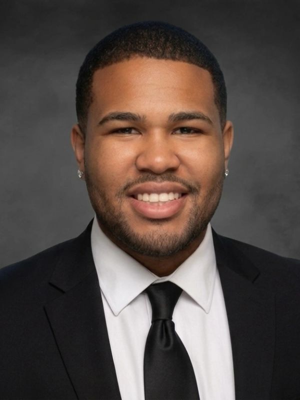 Young man in a black suit and tie smiling.