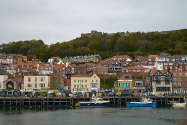 Harbor view with boats, colorful houses, and a hilltop castle in the background.