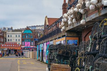 Fishing gear stacked near a street with colorful buildings in the background.