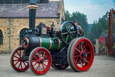 A vintage steam tractor with red wheels and a man operating it outdoors.