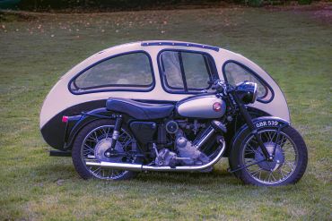 Vintage motorcycle with a unique enclosed sidecar on grass.