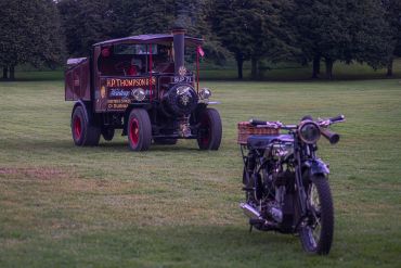 Vintage steam-powered truck and classic motorcycle parked on grass.