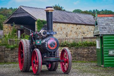 Vintage steam tractor with red wheels in a rustic setting.