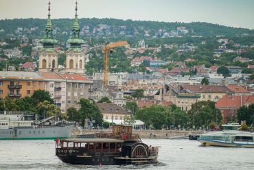 Historic riverboat cruises near a city with twin church towers and green hills.