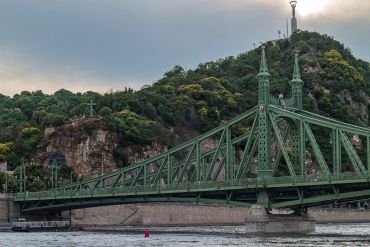 Green steel bridge with hill and statues in the background.